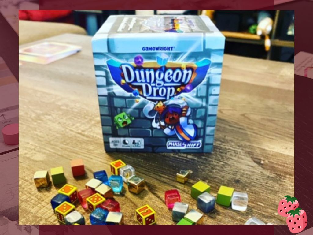 The Dungeon Drop board game box standing on a wooden table with colorful cube components scattered in front, highlighting the game’s compact size and vibrant pieces.