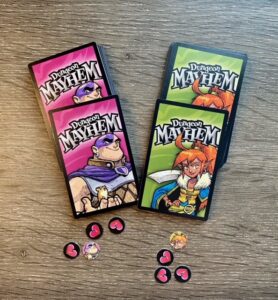 Two Dungeon Mayhem player decks placed side by side on a wooden table, each showing a character card on top, with heart-shaped damage tokens and small character markers placed nearby.
