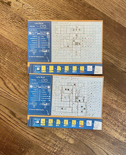 Two completed Floor Plan roll-and-write score sheets filled in with hand-drawn rooms, symbols, and scoring notes, placed side by side on a wooden table.