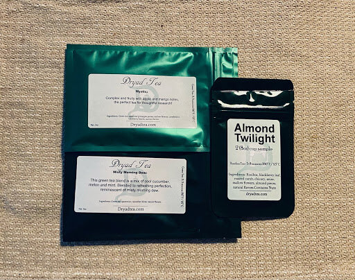 Several Dryad Tea sample packets arranged on a fabric surface, including labeled blends such as ‘Mystic,’ ‘Minty Mending,’ and ‘Almond Twilight,’ highlighting a variety of tea flavors.