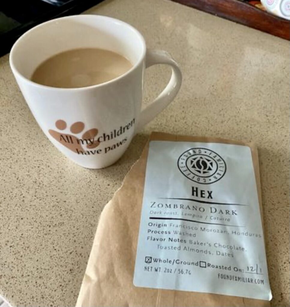 A white ceramic mug filled with coffee sitting on a countertop next to a small bag of Found Familiar Coffee labeled ‘Hex – Zombrano Dark.’ The image highlights the brewed coffee alongside the sample-size package.