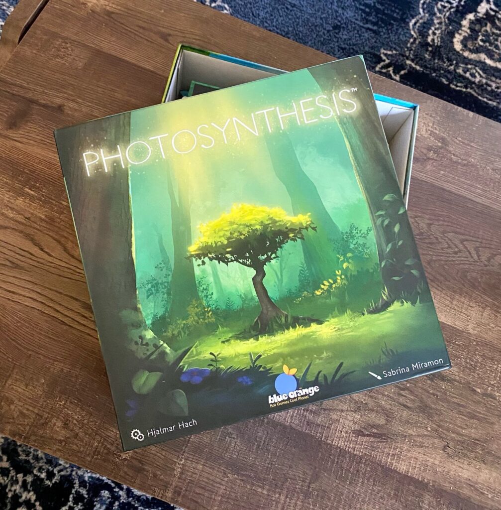 Photosynthesis strategy board game box featuring colorful layered trees and forest artwork, photographed on a wooden table before gameplay.