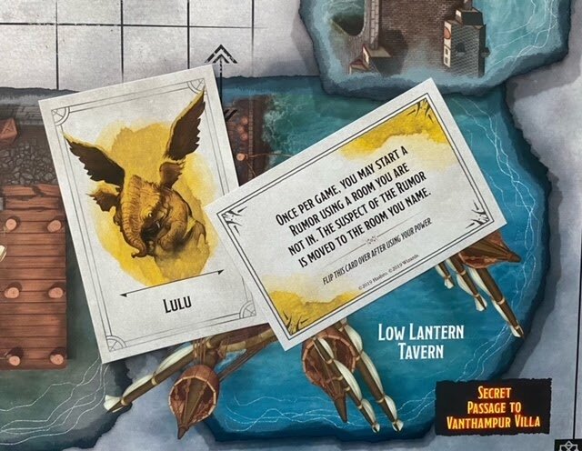 Close-up of Lulu character card and a rumor rule card placed on the Dungeons & Dragons Clue game board at the Low Lantern Tavern location.
