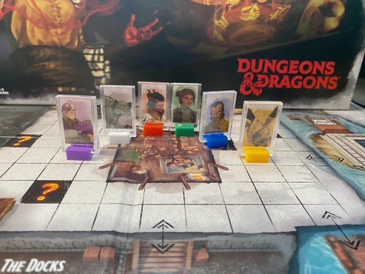 Colorful character standees lined up on the Dungeons & Dragons Clue game board, with the game box visible in the background.