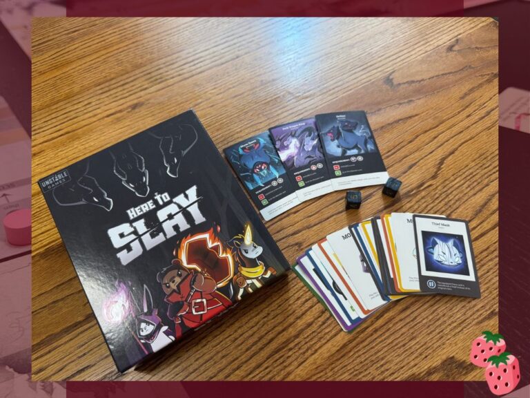 The front of the Game Boy for Here to Slay up Unstable Games is pictured, featuring a warrior bear, a mage bunny and a unicorn with a glowing horn. Next to the box the game cards and dice are spread out.