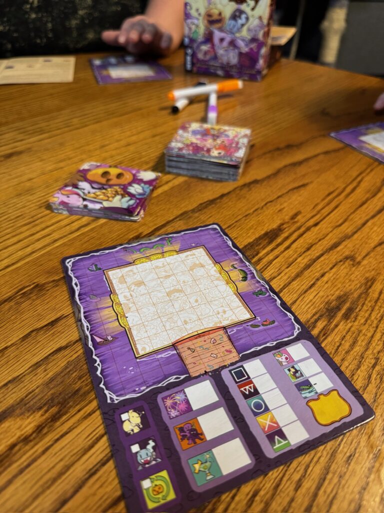 In the foreground you see a blank Castle Party game board. In the background you see a stack of face down cards and a pile of dry erase markers. 