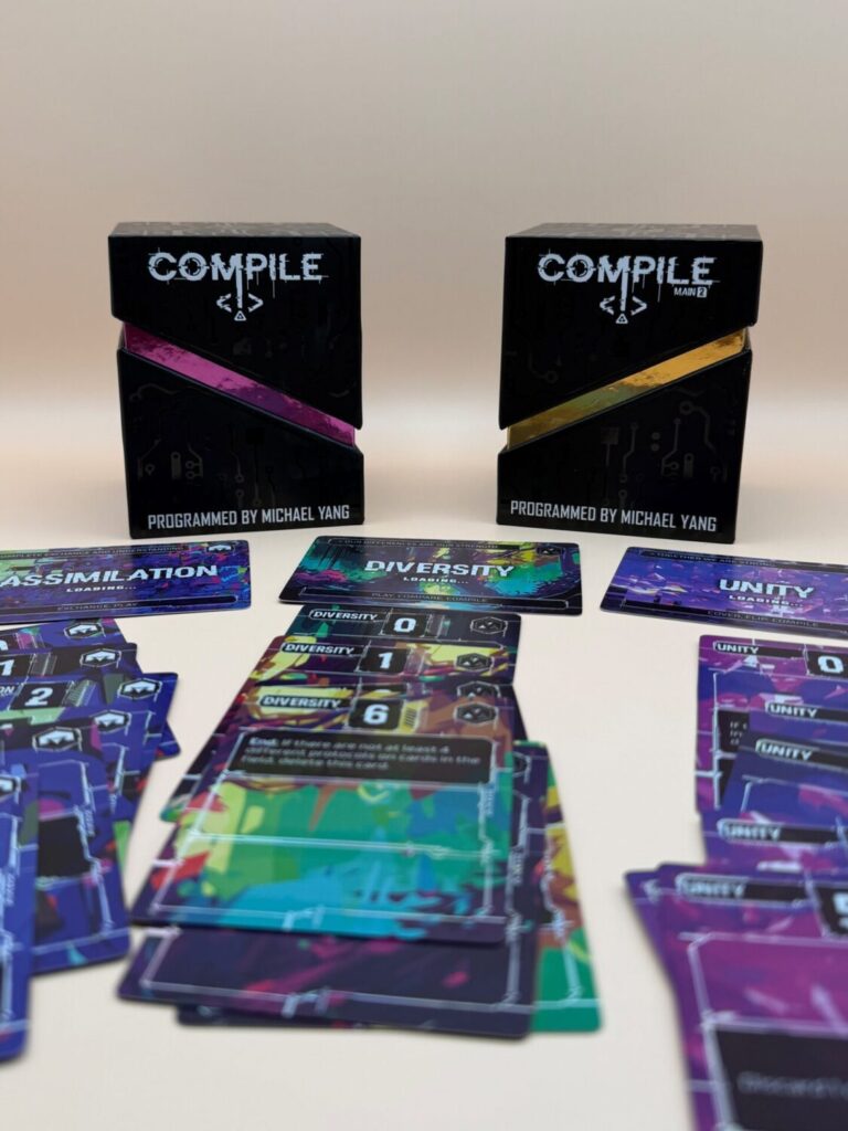 A full shot of the two compile game boxes and three protocols and their cards underneath. The protocols are assimilation, diversity, and unity. The cards are colorful and have holographic accents.