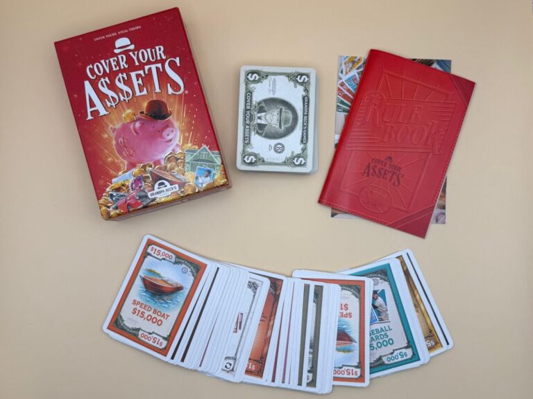 A picture shows the game Cover Your Assets and all of the components. Spread out at the bottom of the picture frame are asses cards. The top card reads Speed Boat 15,000 dollars. Also shown is the reuse book and money cards.