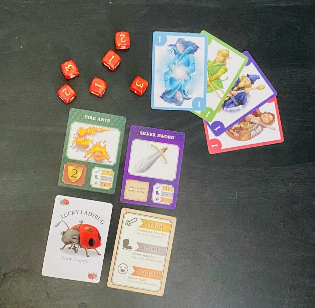 Pieces of the game are laid out indulging 6 six sided dice, 4 numbered playing cards, a fire ants card, a silver sword card, a lucky ladybug card and an action card.