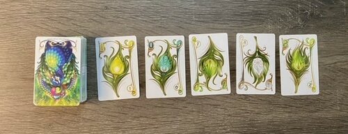 Row of Enchanted Plumes cards featuring a peacock on the far left card. 5 cards of different numbers and colors are shown next to the peacock.