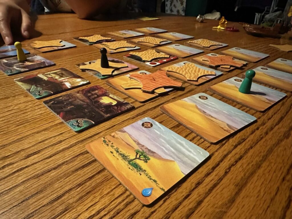 Cardboard space tiles with desert images are set out on a wooden table.