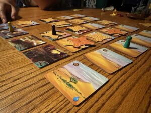 Cardboard space tiles with desert images are set out on a wooden table.