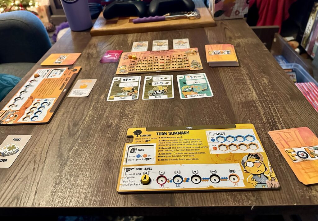 A full table setup of the board game Fort, including player boards with labeled sections, a central victory track with a yellow marker, character cards such as Crash, Blitz, and Golden Boy, and various decks and tokens arranged for active gameplay.