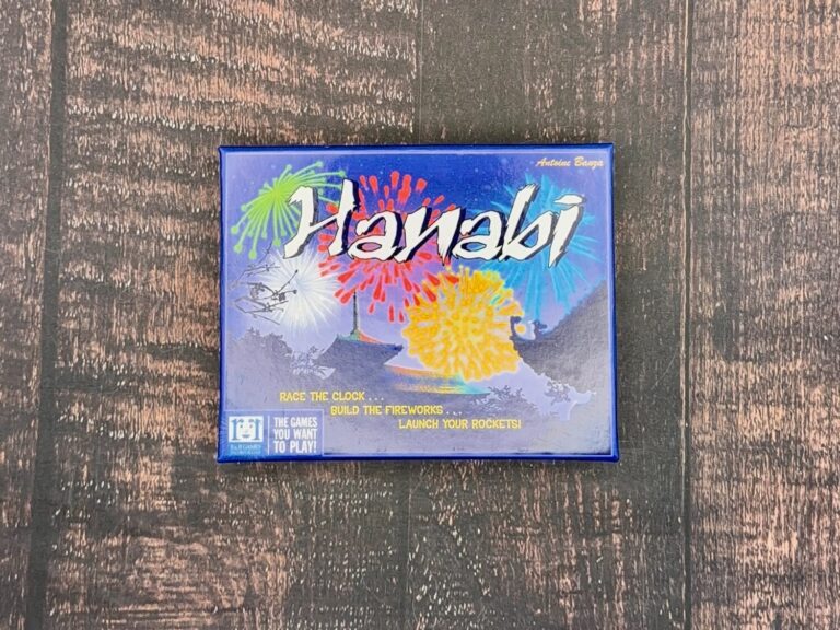 A close up of the Hanabi box cover art. Reads race the clock, build the fireworks, launch your rockets on the bottom. The art shows colorful fireworks in the foreground and a pagoda in the background.