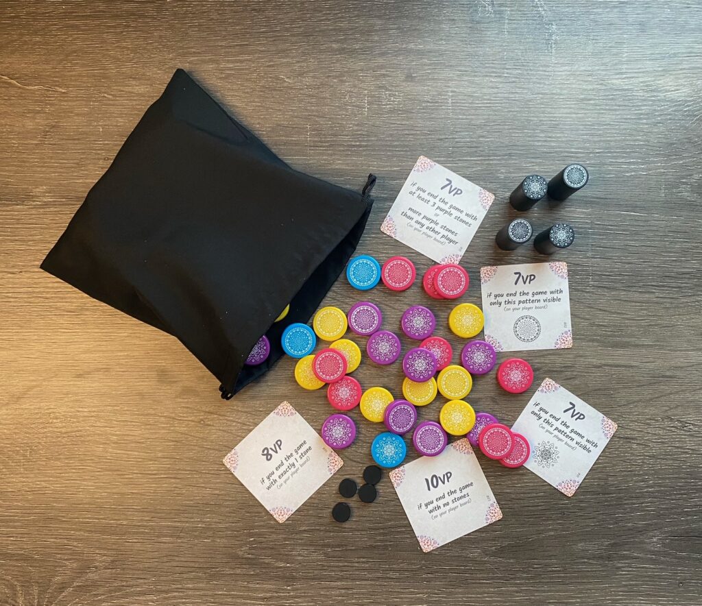 a black drawstring bag has colorful game pieces, black maples, and cards spilling out of it.