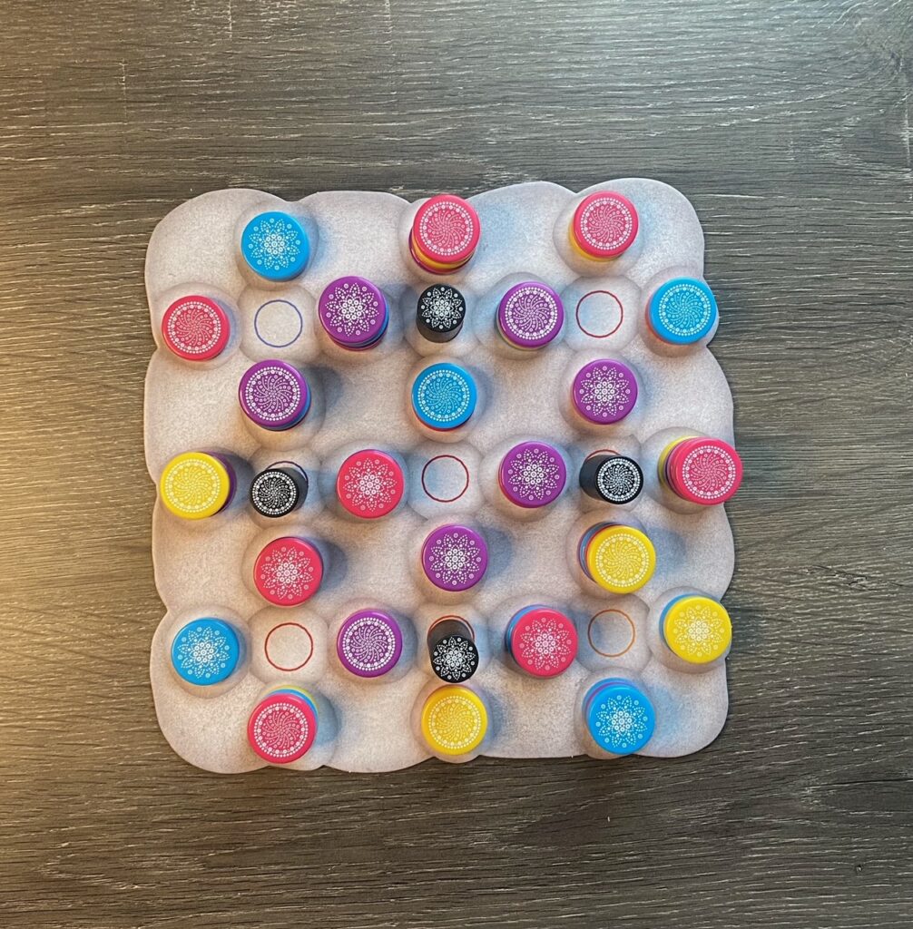 A grayscale game board shows colorful stones and black maples displayed on it, similar to a checkerboard. 