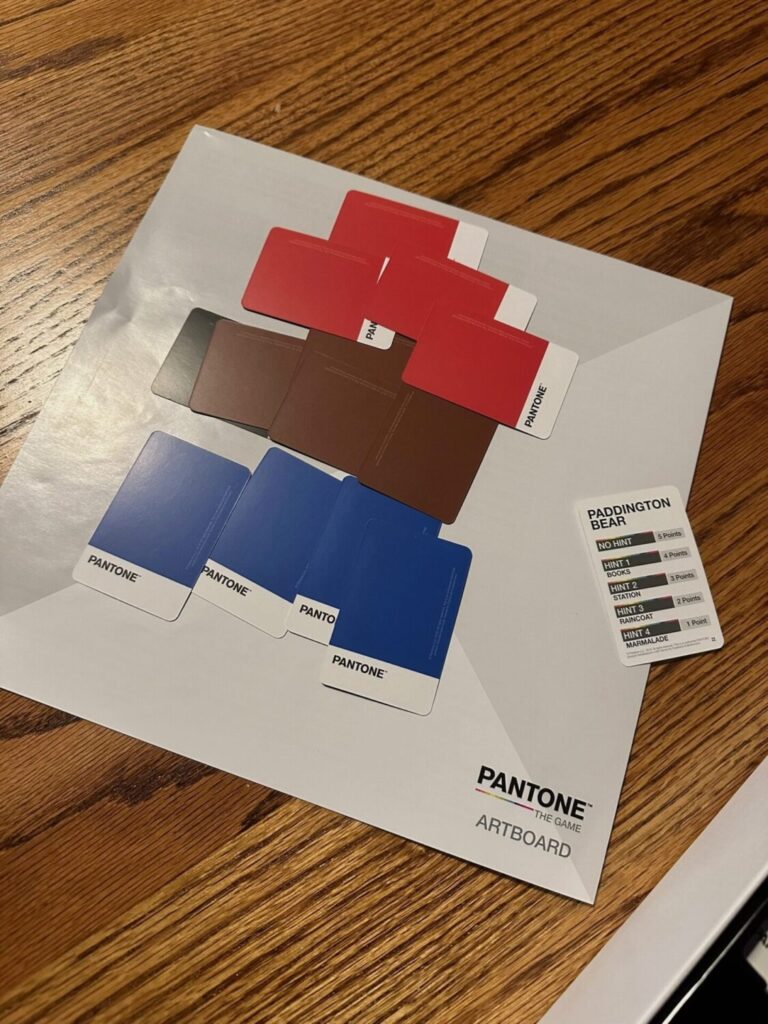 On top of a wooden surface there is a white play area with a card reading paddington bear. Next to it various paint chips make out the approximate shape of paddington bear.