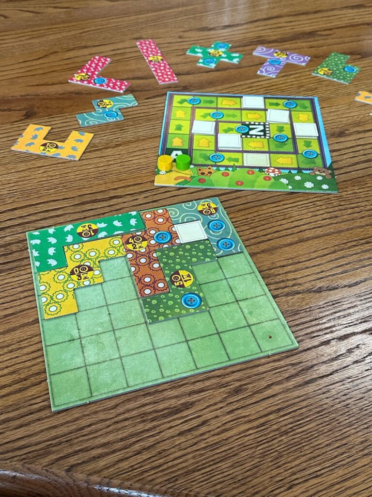A game of Patchwork Express is set up on a wooden table. The board in the front of the frame shows patchwork pieces and buttons on it. In the center shows at board with two meeples and yellow and green arrows. In the background multiple shapes of patchwork are ready to be played. 