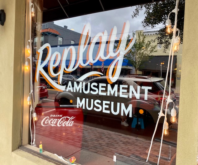On the outside of a window the words Replay Amusement Museum are painted in white.