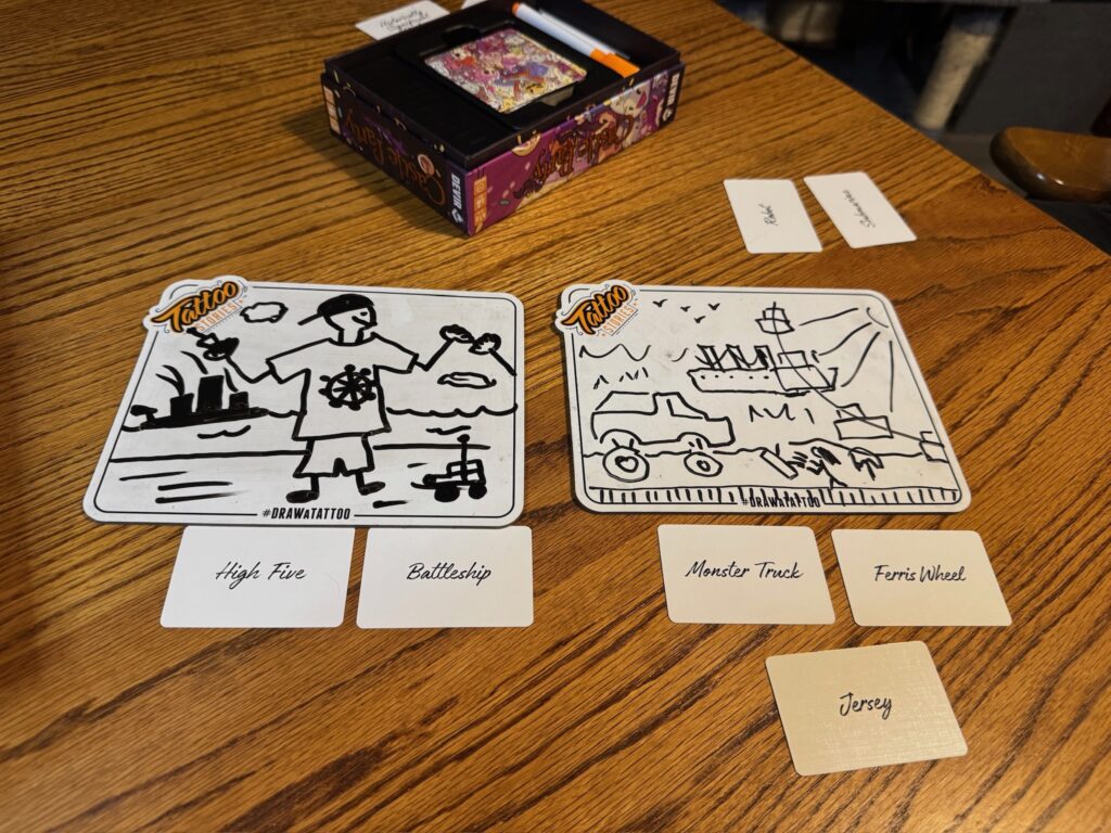 Two small white board picture hand drawn images on the, In front are prompt cards reading high five, battleship, monster truck, ferris wheel and jersey.