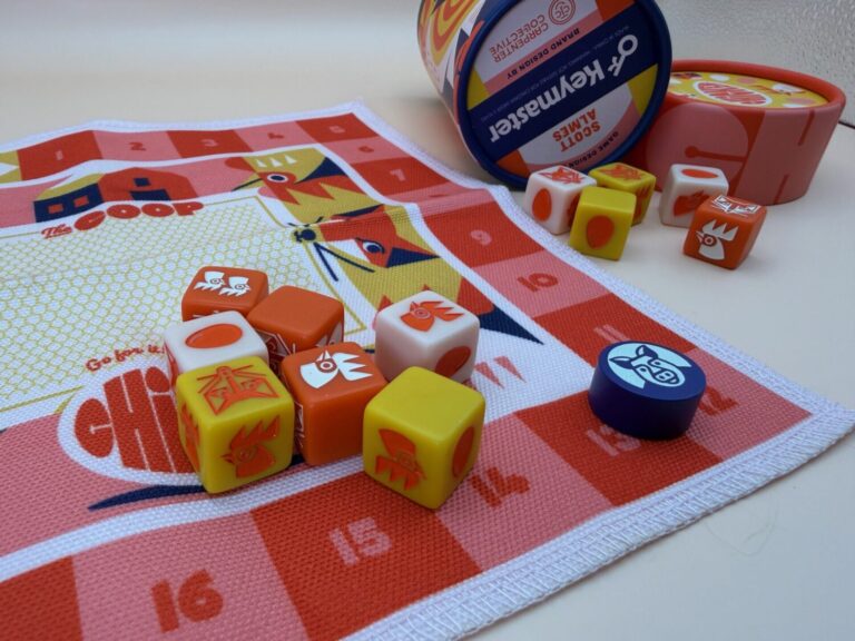 A close up of the game board with dice and a player token in the foreground, and more dice and the game box in the background.