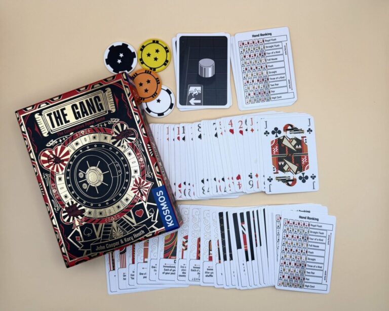 To the left of the frame is a game box labeled The Gang and showing the Kosmos game logo. Pictured on the box is a gold safe, cracked open. The top area of the frame are different colored poker chips with different numbers of stars on them. The rest of the frame is filled with the cards needed to play The Gang and aid cards with hand rankings shown.