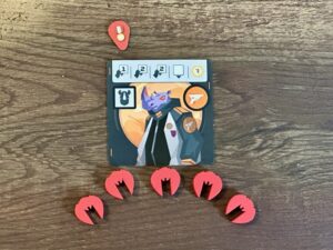 A playing card featuring a rhino dressed like an astronaut sits on a wooden table with five red spaceship tokens sitting underneath. One medal token sits above the card.