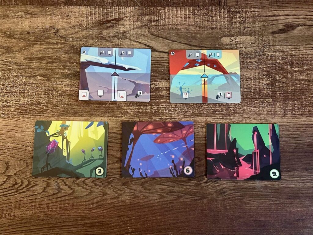 Five game cards picturing different alien lands sit on top of a wooden surface.