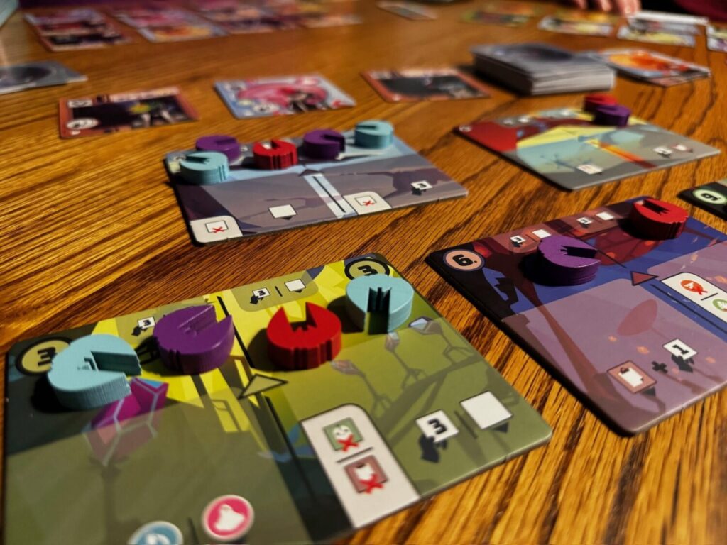 The Wild Space game is speared out on a wooden surface. Colorful, numbered cards are on the playing area, topped with wooden spaceships in blue, red and purple.