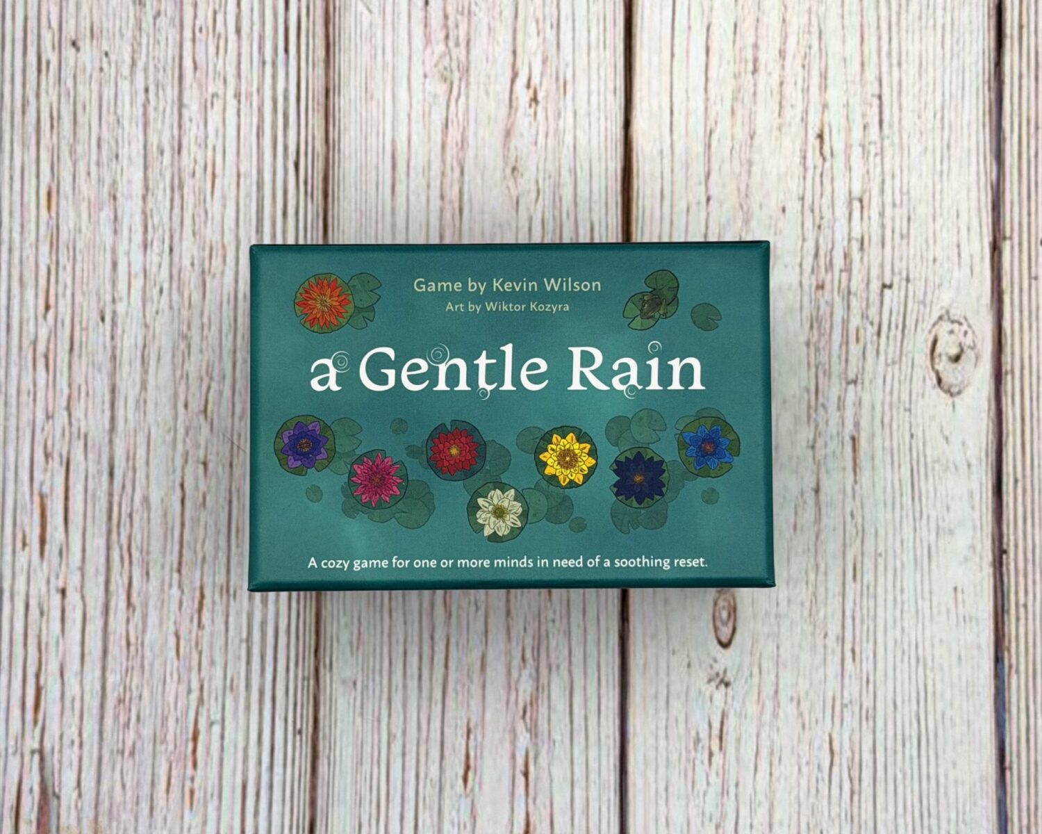 A small blue box sits on a wooden surface. The box is titled A Gentle Rain.
