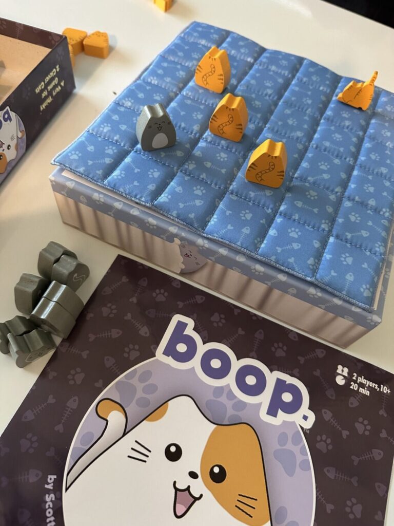 the boop rule book peeks up from the bottom of the image. The top half of the image pictures several cat figures on the quilt. three orange cats are in a diagonal row.