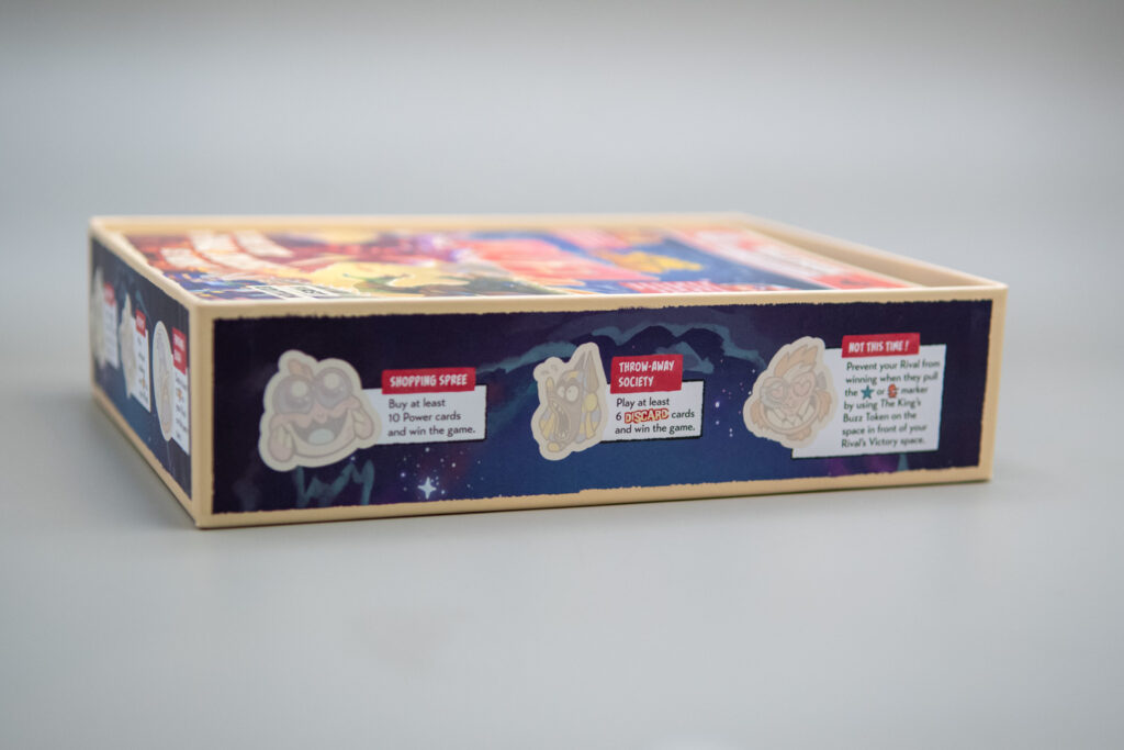 Side view of the King of Tokyo Duel box is shown with light outlines depicting where to put stickers when achievements are met.