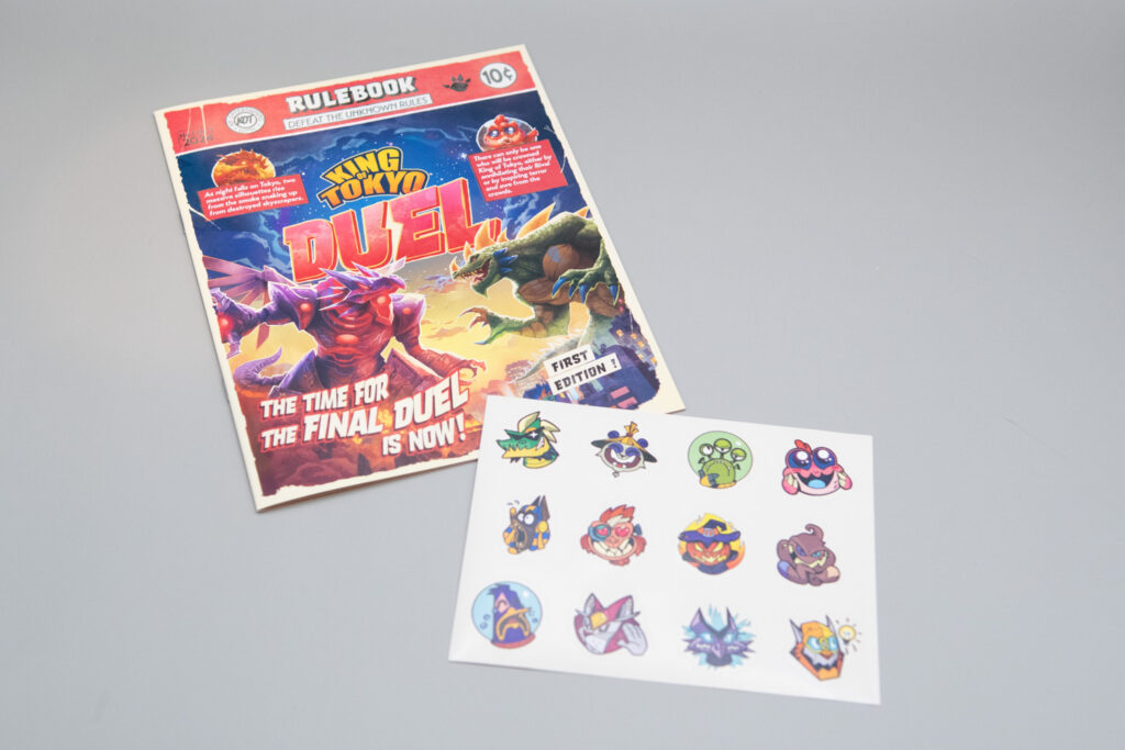 A comic style King of Tokyo rulebook is shown along with some game stickers.