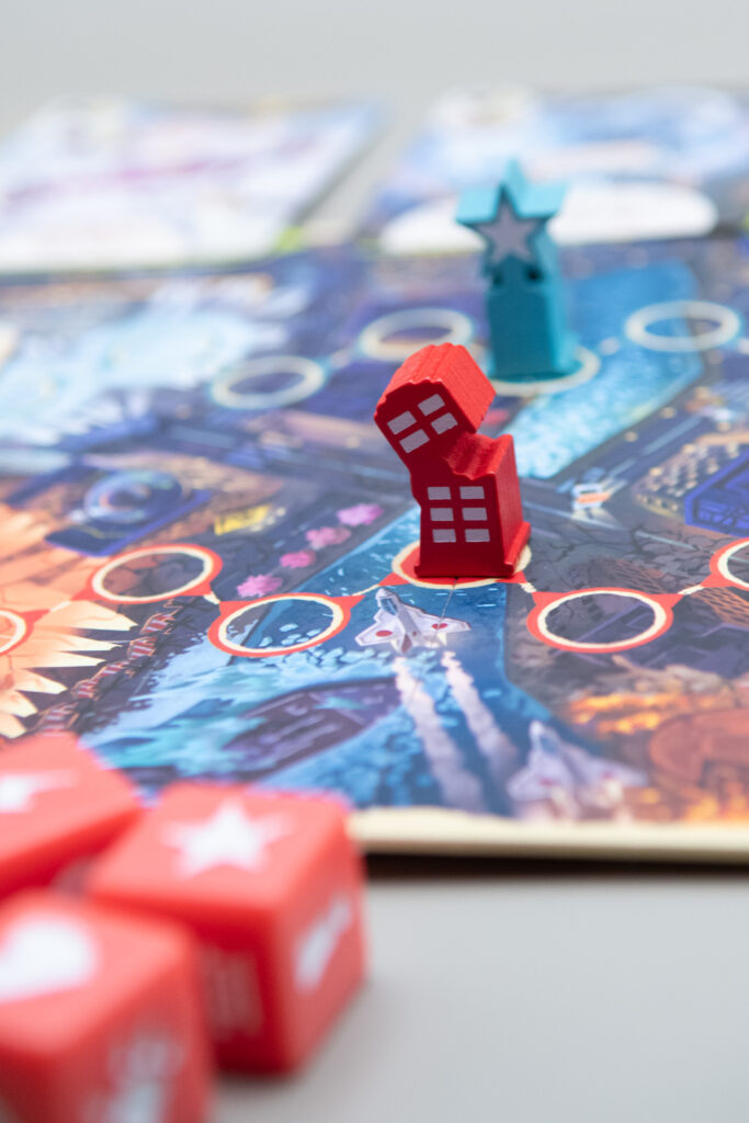 A close up of the King of Tokyo Duel board is shown with the meeple markers in the middle of the board and some dice in the foreground.
