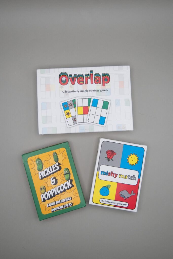 Three card game boxes are on a neutral background. The boxes are titled Overlap, Pickles & Poppycock and mishy match.